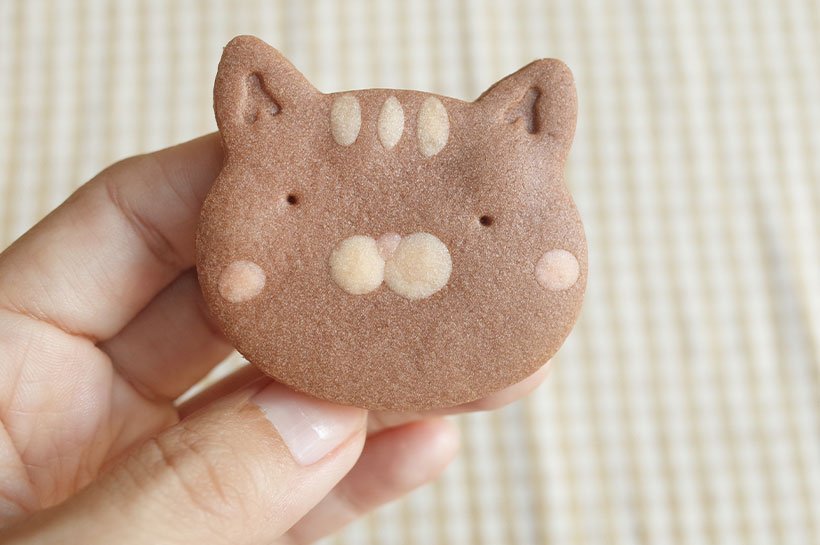 Eine Hand hält einen selbstgebackenen Keks in Form eines Katzenkopfes.