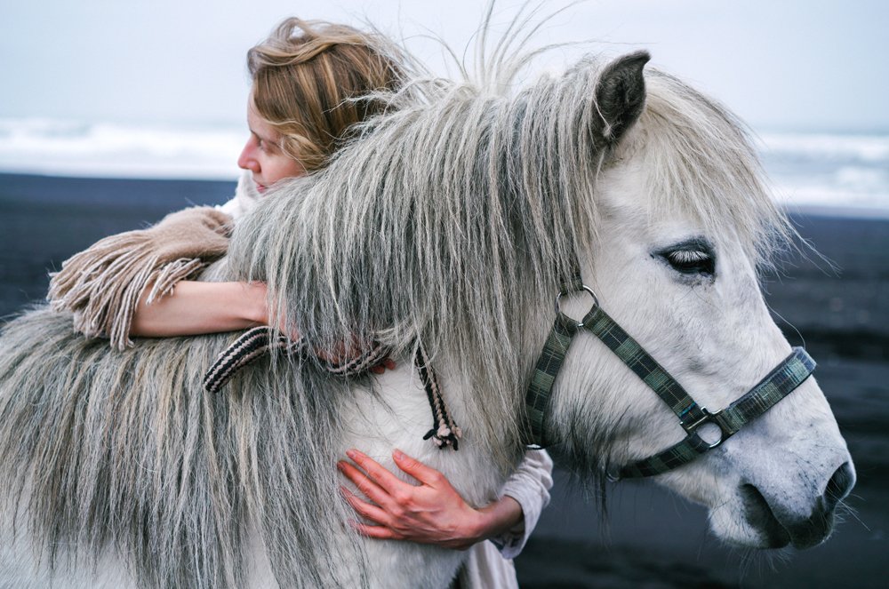 Eine Frau kuschelt mit einem Pony mit dickem Winterfell.
