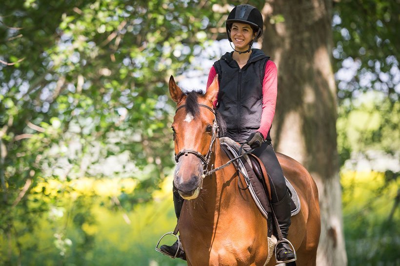 Frau reitet ruhig im Gelände mit Helm auf dem Kopf